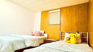 Una habitación con dos camas, paneles de madera en las paredes, una ventana con persianas y una mesita.