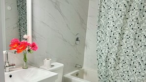 Un baño con lavamanos, inodoro y bañera blancos, un espejo y una cortina de ducha con diseño de mosaico.