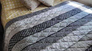Un letto con copripiumino a quadri, cuscini decorati e una coperta con motivi geometrici.