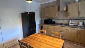 Eine Küche mit Holztisch und -stühlen, einem schwarzen Kühlschrank, Holzschränken und einem Gasherd.