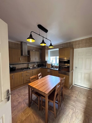 Een keuken met houten kastjes, een eettafel met stoelen en een ingebouwde oven.
