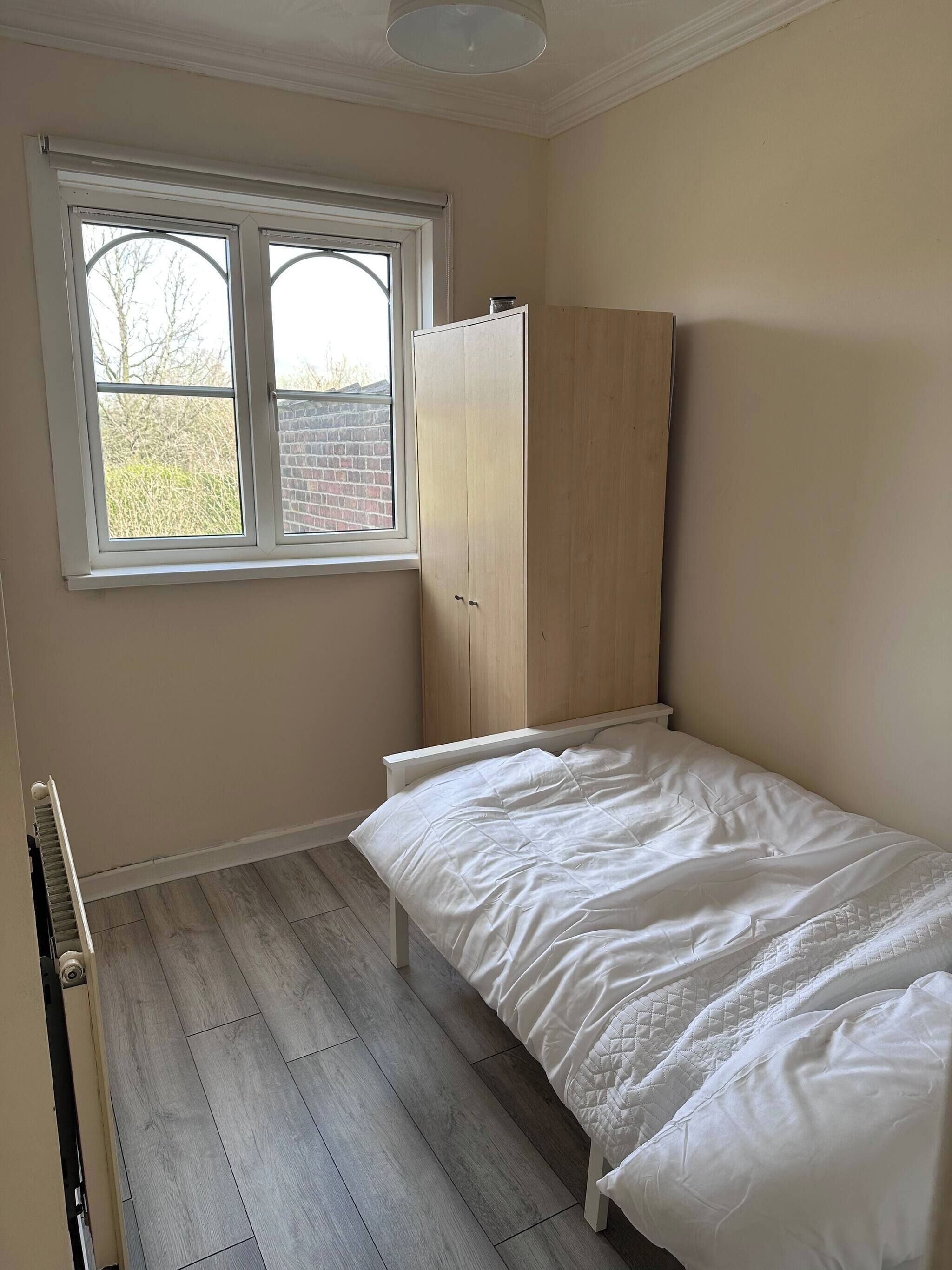 A bedroom with a bed, a wardrobe, a window, and a radiator.