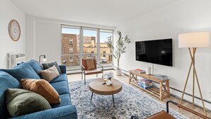 A modern living room with a sofa, a coffee table, a TV, and a large window. - Wonderful 1BR Retreat with Balcony in Oak Park (Oak Park)