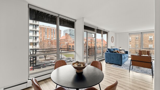 A modern apartment with a dining area, a living room with a blue sofa, and large windows offering city views. - Wonderful 1BR Retreat with Balcony in Oak Park (Oak Park)