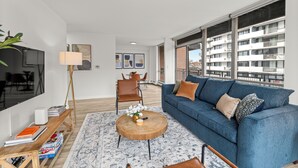 A modern living room with a blue sofa, a round coffee table, a TV, and a dining area with chairs and a table. - Wonderful 1BR Retreat with Balcony in Oak Park (Oak Park)