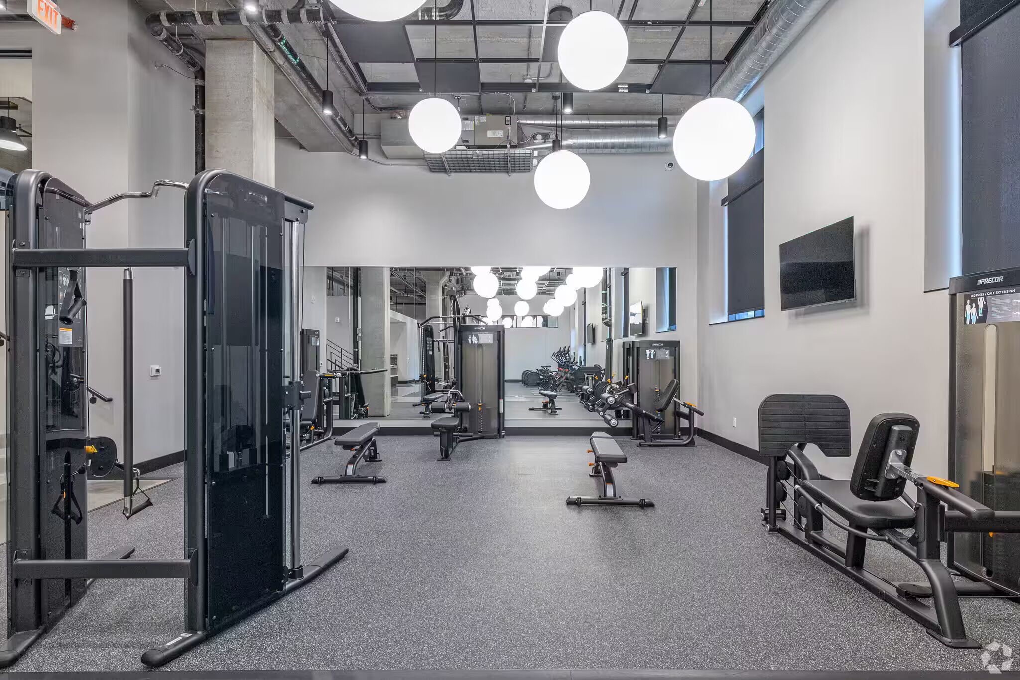 A gym with exercise equipment, a mirror, and a television on the wall.