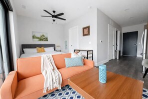 Ein modernes Hotelzimmer mit Bett, orangefarbenem Sofa, Holz-Couchtisch und Deckenventilator.