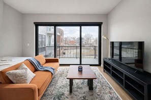 Een moderne woonkamer met een bank, een salontafel, een televisie en een balkon met uitzicht op gebouwen.