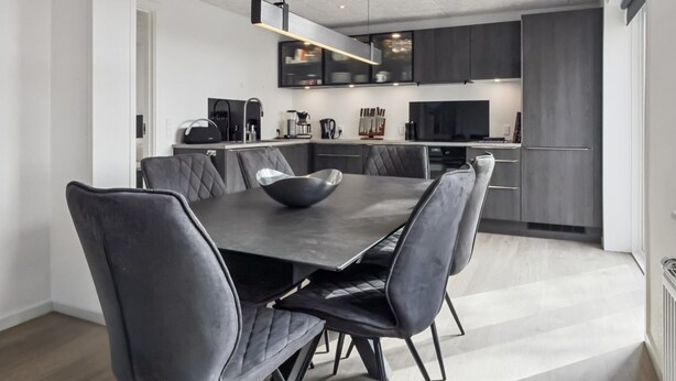 A modern kitchen with dark cabinets, a dining table with six chairs, and a large black bowl on the table. - "Milan" - 20km from the sea by Interhome (Bredebro)