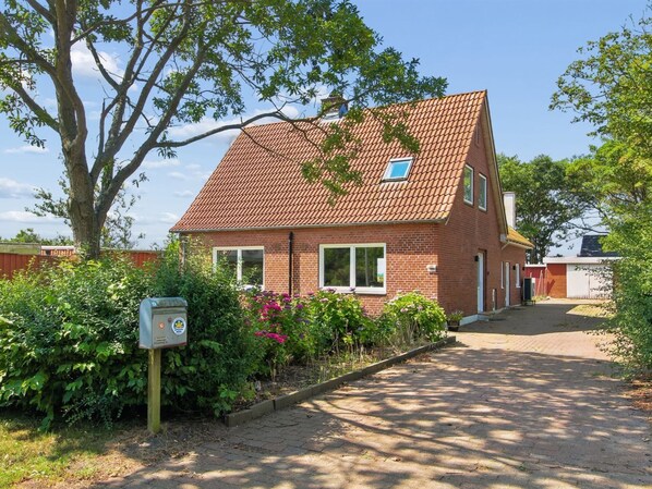 A brick house with a tiled roof, a small window, and a garden with flowers.