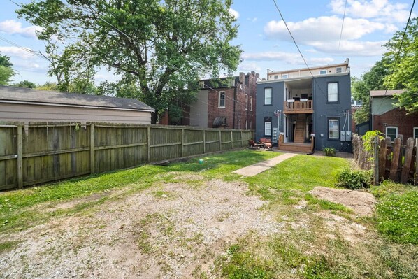 A backyard with a wooden fence, a grassy area, and a two-story building with a balcony.