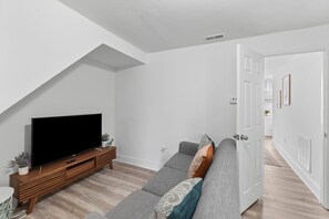 Ein modernes Wohnzimmer mit Flachbildfernseher, grauem Sofa, einer Holzunterhaltungsecke und einer weißen Tür.