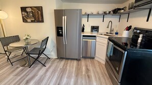 Une cuisine moderne équipée d’un réfrigérateur, d’un four et d’un lave-vaisselle. On y trouve une table à manger avec des chaises et un tableau accroché au mur.