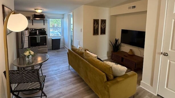 Un salon moderne avec un canapé, une table à manger et des chaises, un téléviseur, et un coin cuisine à l’arrière-plan.
