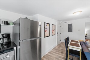 Eine kompakte Küche mit einem Edelstahl-Kühlschrank, einer Kaffeemaschine und einem Geschirrspüler. Es gibt eine Essecke mit Tisch und Stühlen.