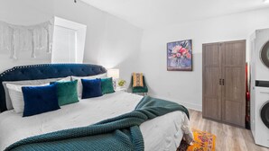 Un dormitorio con cama, armario, lavadora y un cuadro en la pared.