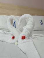 Uma cama com toalhas brancas dispostas em formato de coração, cada toalha com um logotipo e uma rosa vermelha.