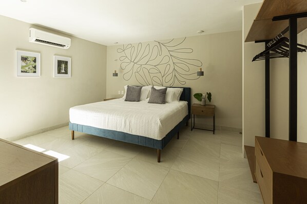 Ein Schlafzimmer mit Bett, Nachttischen, einer Wand-Klimaanlage und einer hölzernen Sitzbank.