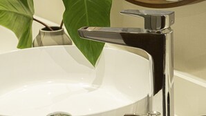 Un lavabo blanc avec un robinet chromé, un miroir et une plante en pot dans une salle de bain.