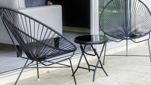 Un espace de vie moderne comprenant un canapé, deux fauteuils, une petite table, un téléviseur et une porte-fenêtre coulissante donnant sur un jardin.