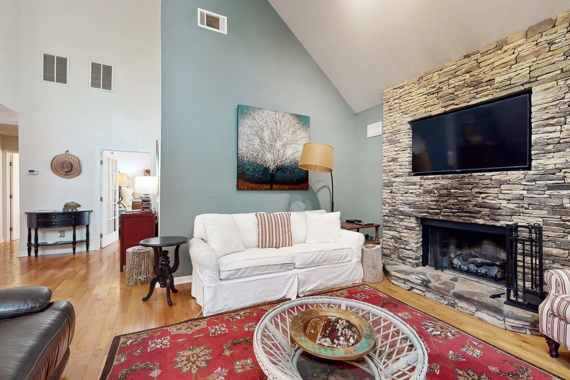 Una sala de estar con chimenea de piedra, un sofá blanco, un cuadro y un televisor montado en la pared.