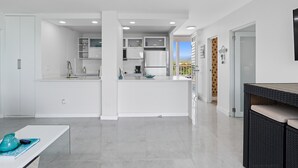 Una cocina moderna con armarios blancos, una isla central y un comedor con una mesa de mimbre negra.