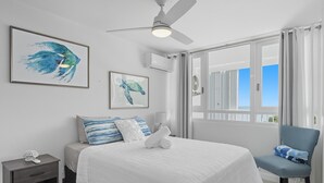 Un dormitorio con cama, una silla, una mesita de noche, ventilador de techo y obras de arte en las paredes.
