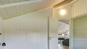 Un dormitorio con cama, mesita de noche, puerta que da a un comedor y techo con vigas de madera.