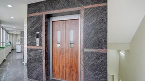 A hallway with a marble floor, a wooden elevator door, and a green counter. - Deluxe the Paradise Guest inn (Nellore)