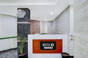A reception desk with a 'HOTELO' sign, a potted plant, and a wall-mounted fan. - Deluxe the Paradise Guest inn (Nellore)