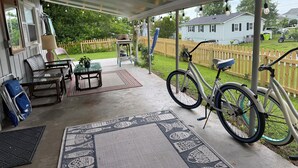 Een overdekt terras met een tafel, stoelen, een fiets en uitzicht op een huis op de achtergrond.
