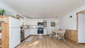Een moderne keuken met witte kasten, een inbouwoven en een eethoek met een houten tafel en stoelen.