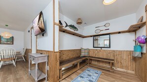 Een kamer met een houten bankje, een kleine tafel, een televisie en een spiegel aan de muur.