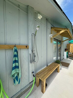 Un banc en bois, une serviette et une pomme de douche adossés à un mur d’immeuble.