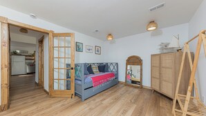 Een kamer met een bed, houten vloeren, een kledingkast en een klein keukenhoekje op de achtergrond.