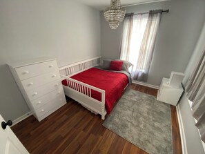 Un dormitorio con cama blanca, cómoda, alfombra gris y candelabro.