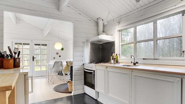 Une cuisine moderne avec des meubles blancs, une grande fenêtre et un coin repas comprenant une chaise et une petite table.