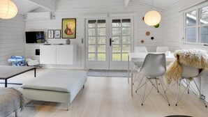 Un intérieur moderne aux couleurs claires, avec un espace repas, un canapé, un téléviseur et des œuvres d’art accrochées au mur.