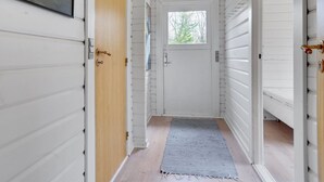 Un couloir aux murs recouverts de lambris blancs, une porte en bois, une fenêtre et un luminaire.