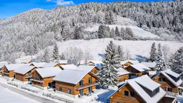 Un groupe de chalets en bois aux toits inclinés, entourés d’arbres couverts de neige et avec une montagne en arrière-plan.