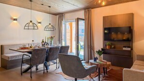 Un espace de repas moderne avec un plafond en bois, des luminaires suspendus, une table à manger entourée de chaises et une vue sur l’extérieur.