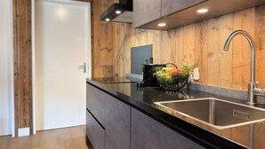 Une cuisine moderne avec des murs en bois, un plan de travail noir, un évier en acier inoxydable et un panier de fruits.