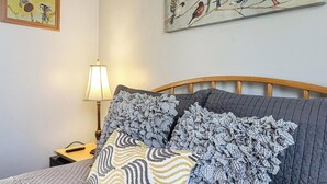Un letto con copripiumino trapuntato grigio, due cuscini decorati, una testiera in legno, un comodino con una lampada e un quadro con uccelli appeso al muro.