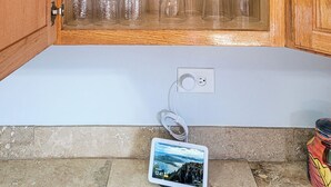 Un mobiletto in legno con ripiani che contengono bicchieri e barattoli, un tablet a terra e una presa elettrica.