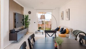 Una sala de estar moderna con televisor, sofá, mesa de comedor, sillas y un balcón con vistas.