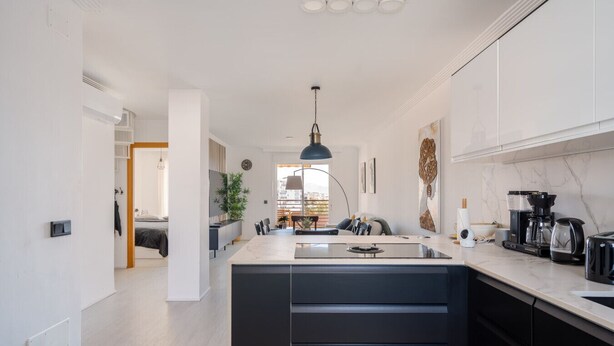 Una cocina moderna con una isla central, armarios negros y una lámpara colgante.