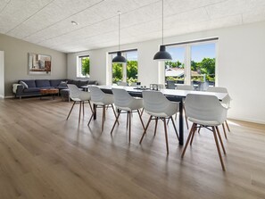 Een moderne keuken met een eethoek, grote ramen, en een woonkamer met een bank en salontafel.