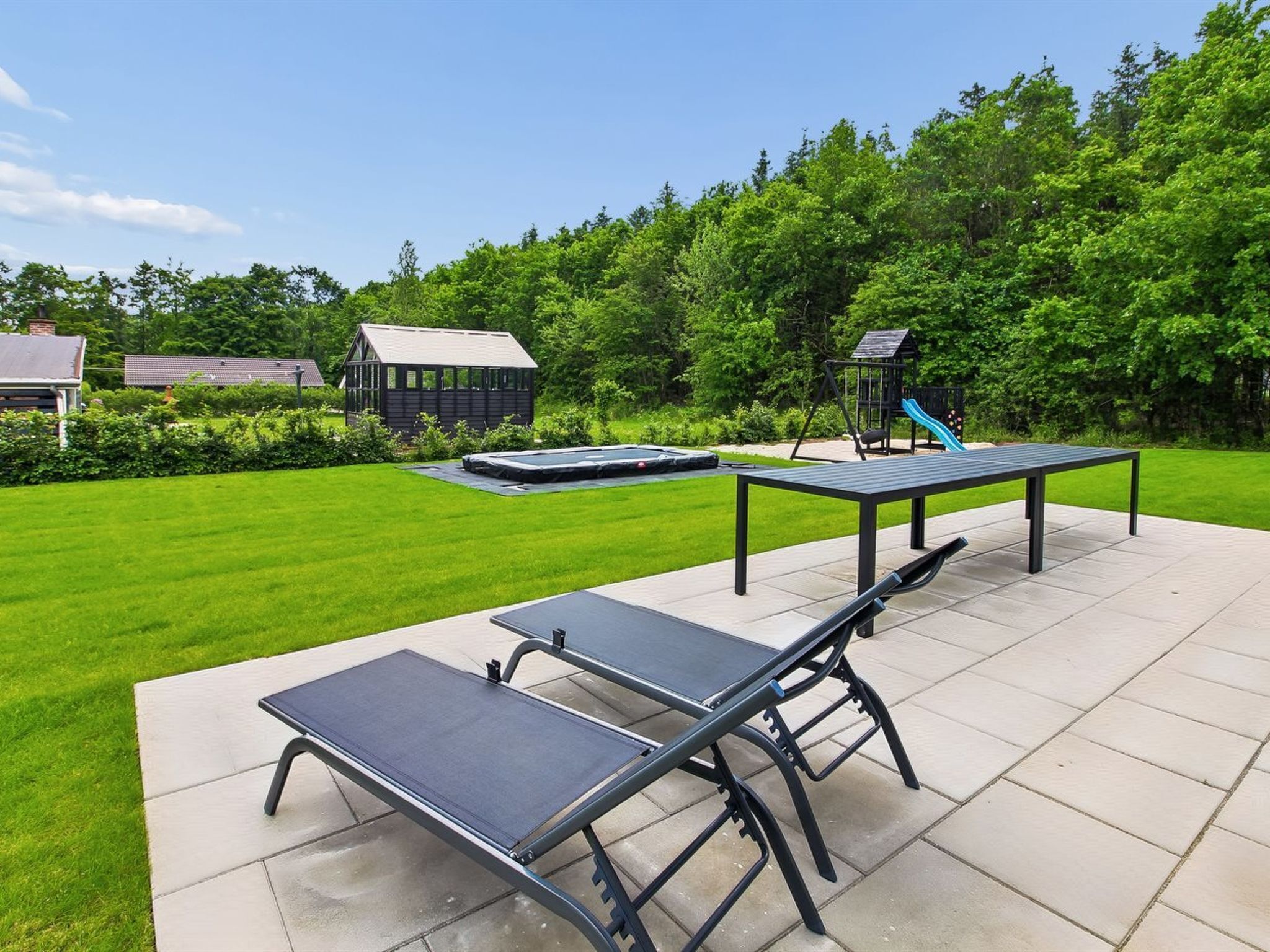 An outdoor patio with a table and benches, surrounded by a well-maintained lawn and trees.