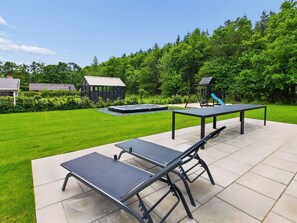 Eine Terrasse im Freien mit Tisch und Bänken, umgeben von einem gepflegten Rasen und Bäumen.