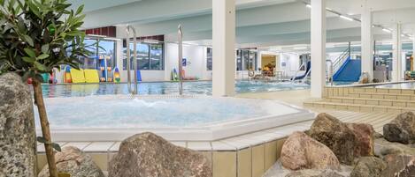 An indoor swimming pool with a hot tub, surrounded by rocks and a potted plant.